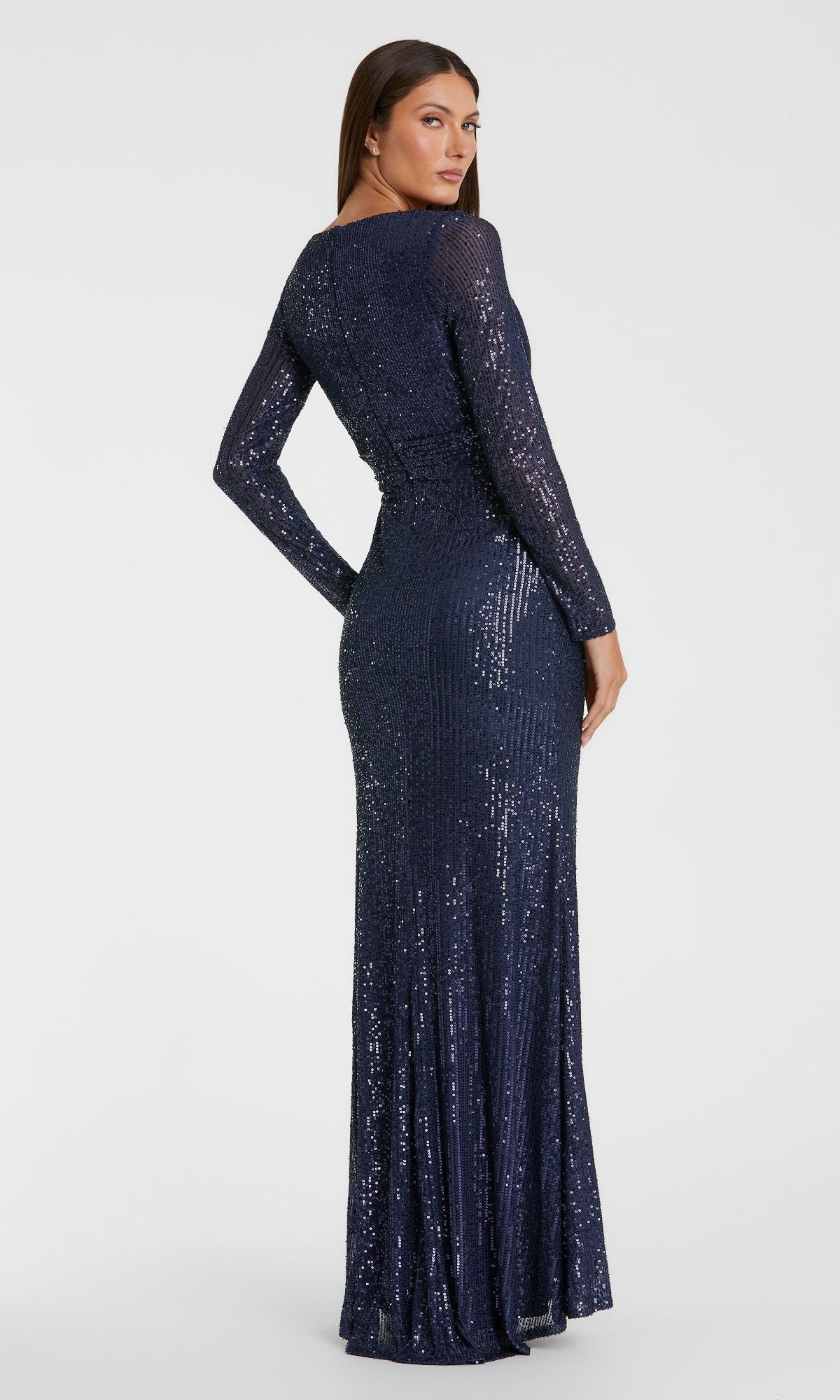 A woman stands with her back turned, head slightly to the side, modeling the Mac Duggal 26490 long-sleeve formal dress covered in navy blue sequins against a plain background.